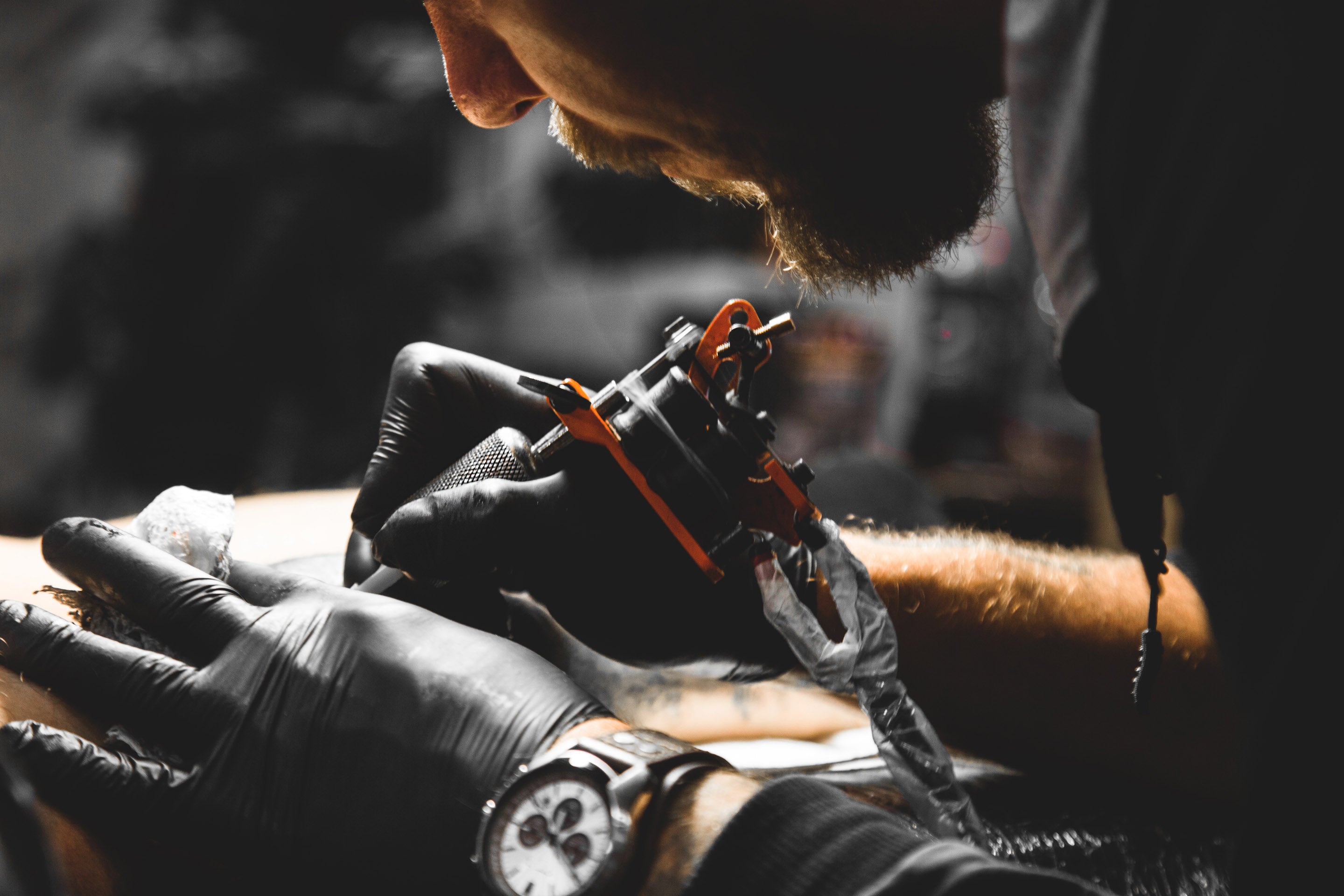 Tattoo artist wearing black gloves tattooing client. 